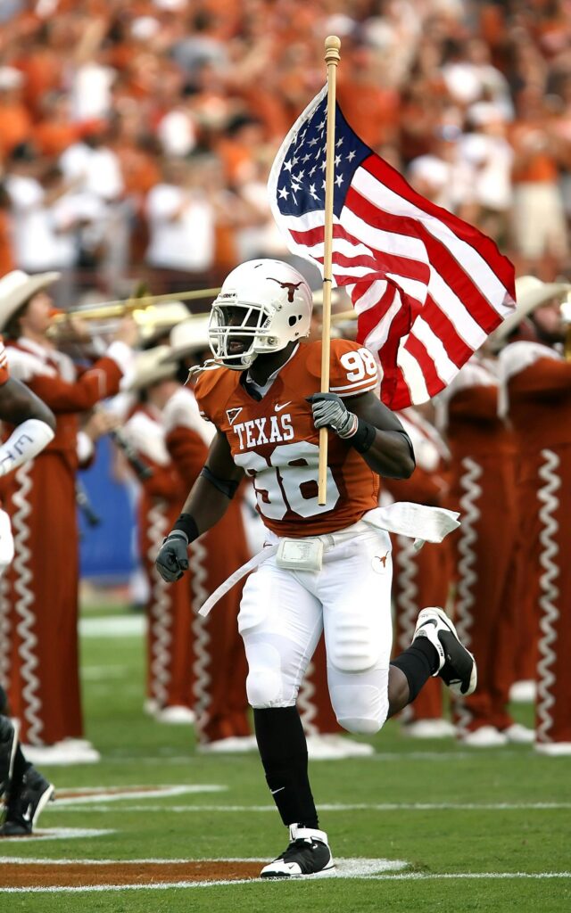 The CFP Is Broken: Say Goodbye to Non-Conference Games Football player runs with American flag at a Texas game, showcasing team spirit and national pride.