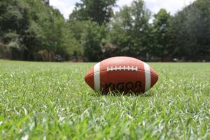 A close-up of an American football on a grassy field, highlighting outdoor sports in summer.
